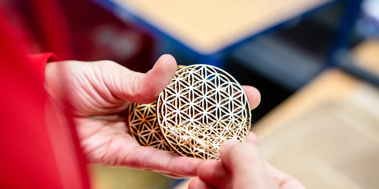 Una persona tiene in mano dei sottobicchieri in legno dal taglio intricato, realizzati con la fresa laser Trotec CO₂.